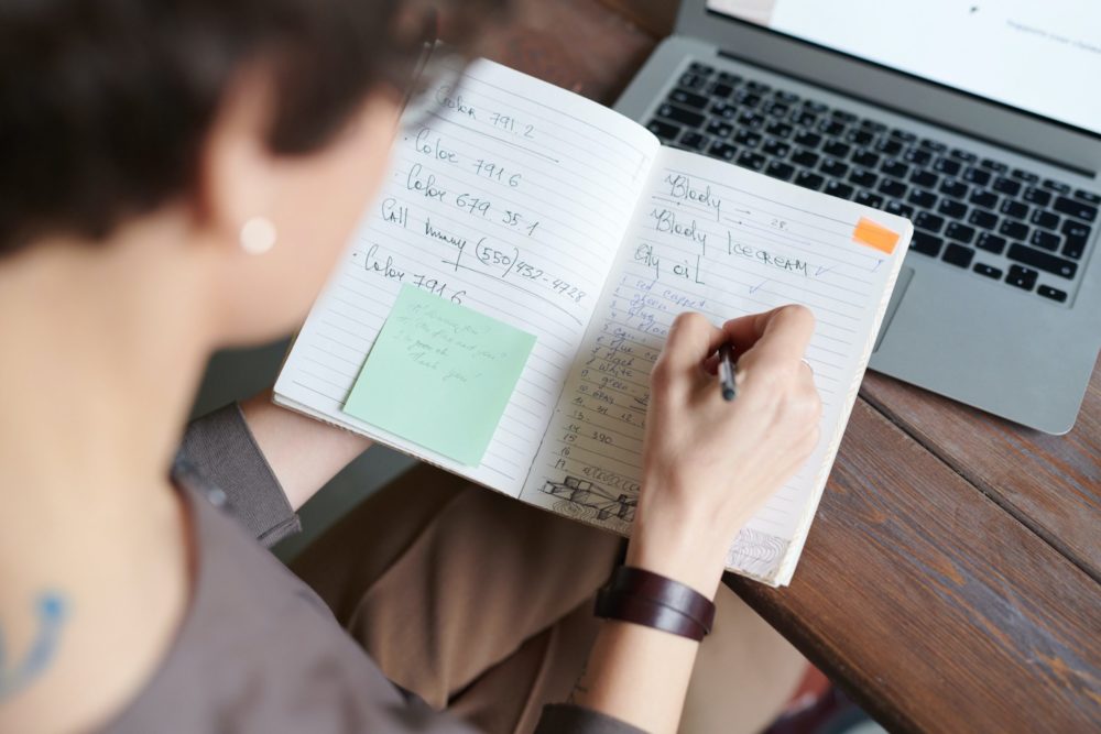 woman writing down notes on a notebook at a desk