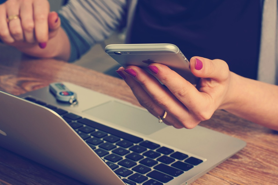 woman hand holding a cellphone sitting at a laptop