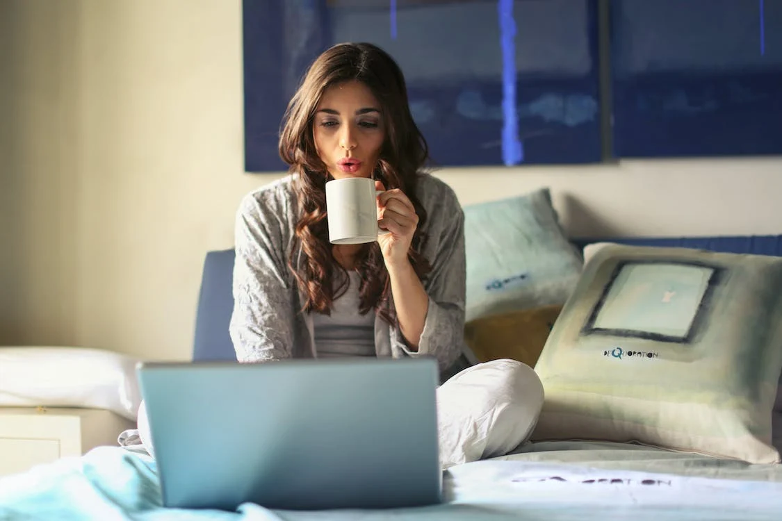 woman with a coffee cup working on her bed