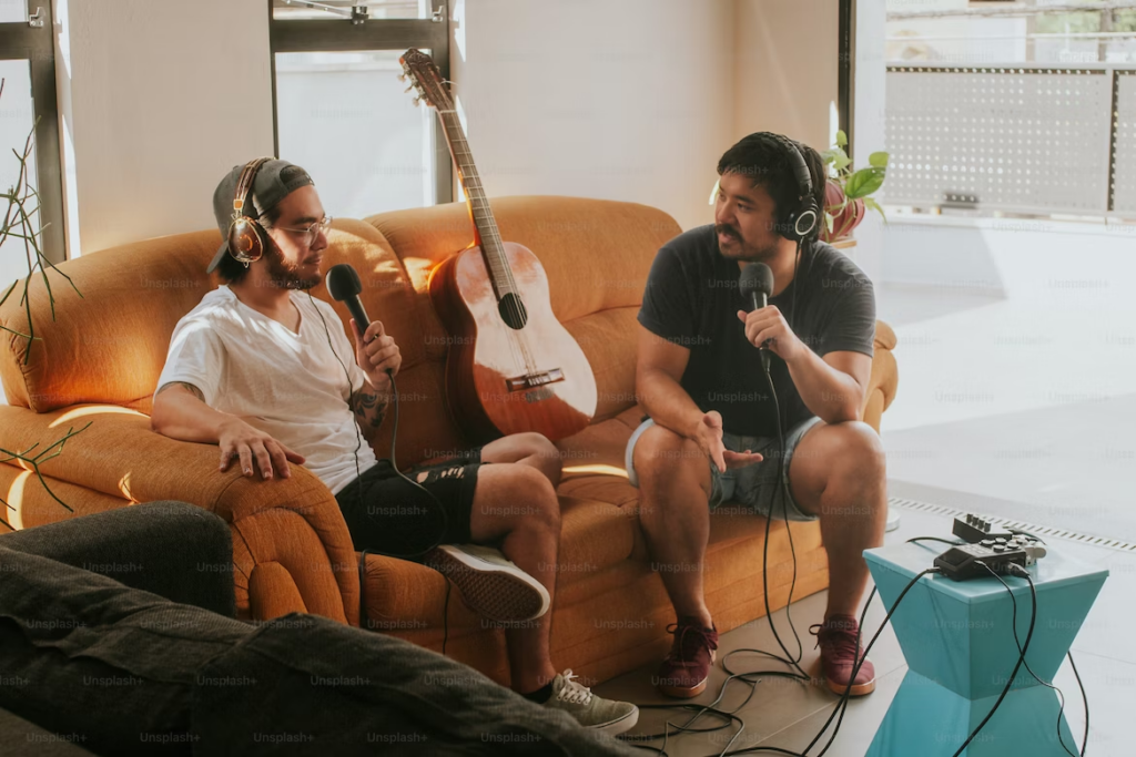 two men doing a music podcast with a guitar between them on a couch